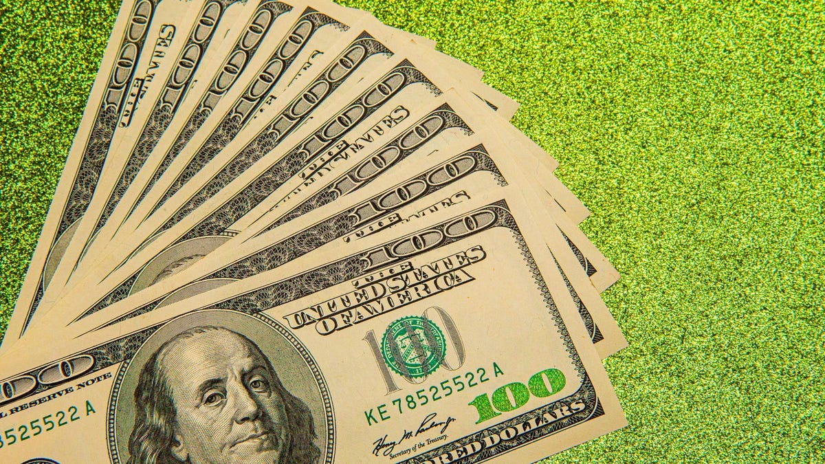 A stack of hundred dollar bills are laid out on a green background.