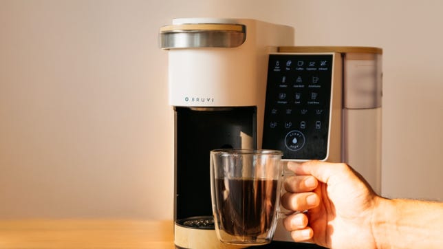 hand holding cup of coffee in front of bruvi machine