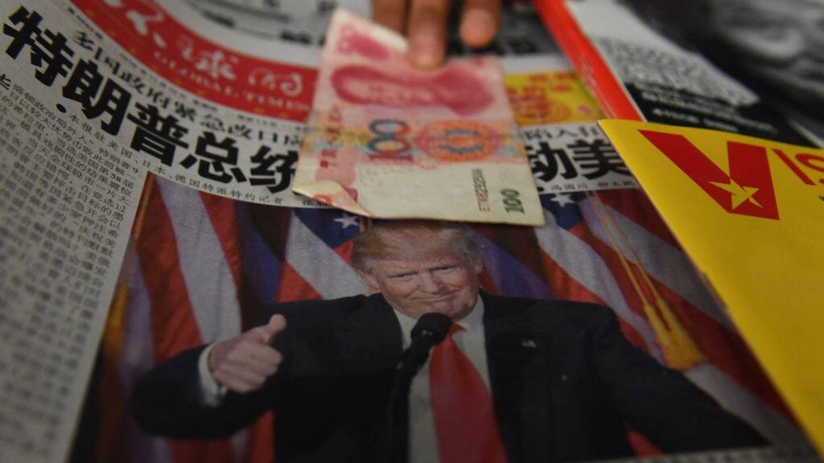 A vendor picks up a 100 yuan note above a Chinese language newspaper featuring a photo of Donald Trump, at a newsstand in Beijing