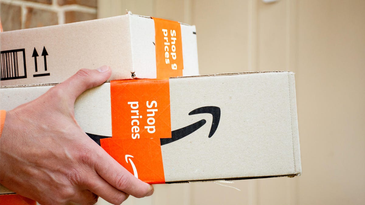 Hands hold two brown Amazon boxes in front of a door.