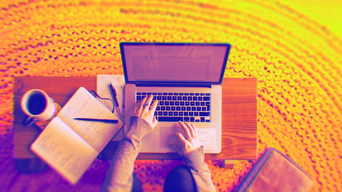 hands on a laptop typing at a desk with a notepad and coffee cup
